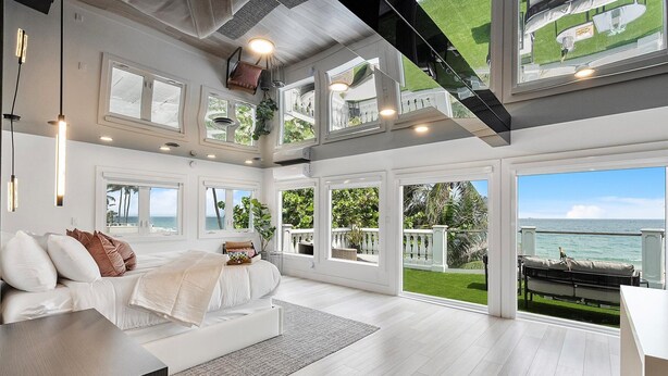 A spacious bedroom with a large bed, multiple windows, and a view of the ocean.