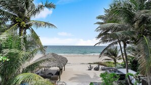 A beach view with a wooden deck, lounge chairs, and a thatched roof structure.