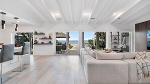 A spacious living area with a large window offering a view of the ocean, a cozy seating area with a sofa and a coffee table, and a dining area with chairs and a table.