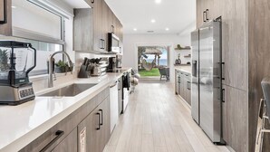 A modern kitchen with stainless steel appliances, wooden cabinets, and a view to a patio with a hammock.