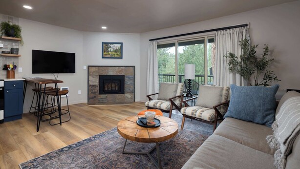 Una sala de estar con chimenea, televisor, sofá y un comedor con taburetes de bar.