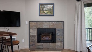 Una sala de estar con chimenea de piedra, televisor montado y comedor con taburetes.