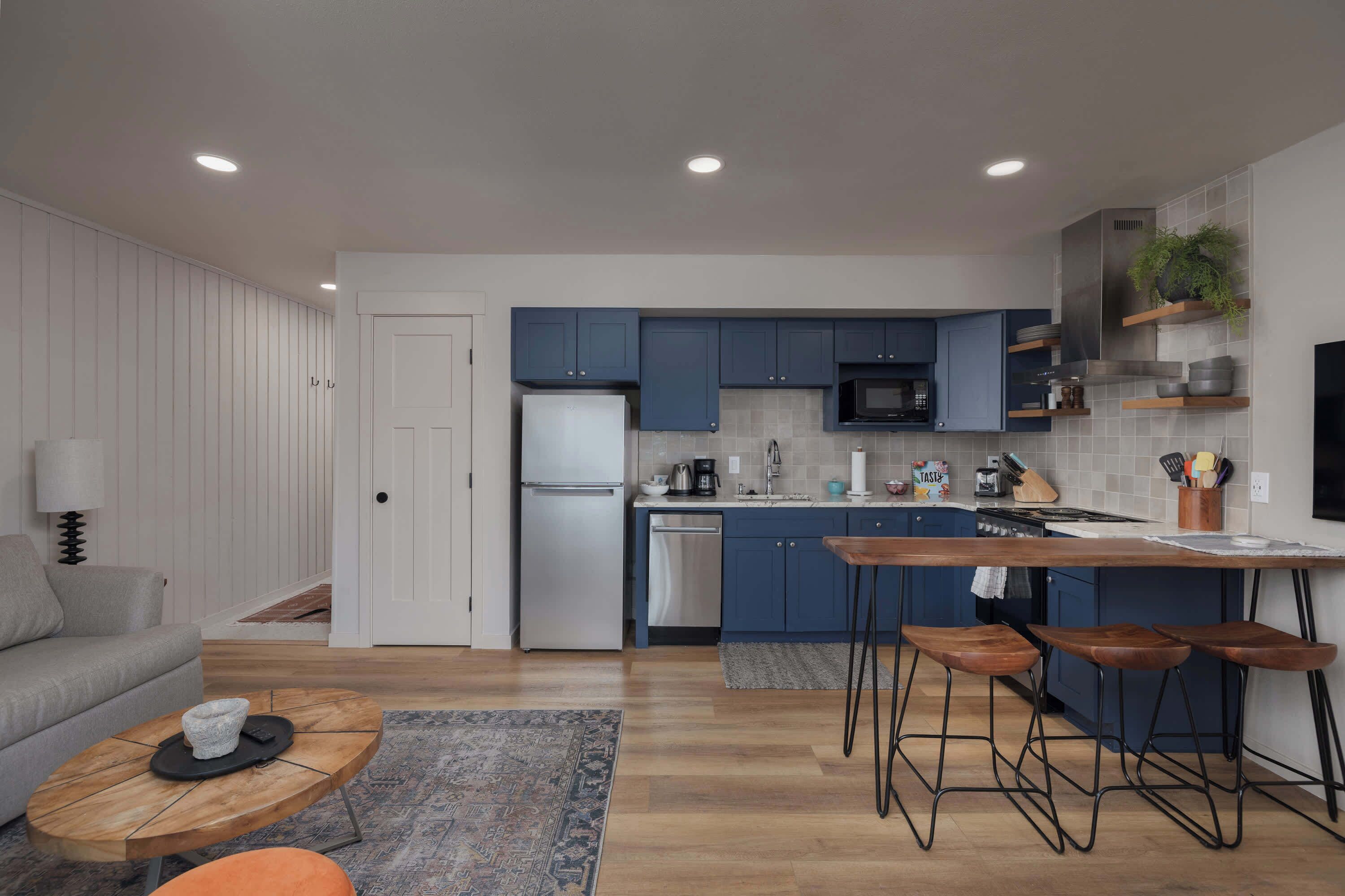 A modern kitchen with blue cabinets, a central island with stools, and a refrigerator.