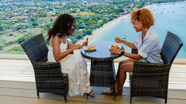 Zwei Personen essen an einem Tisch mit Blick auf Strand und Stadtlandschaft.