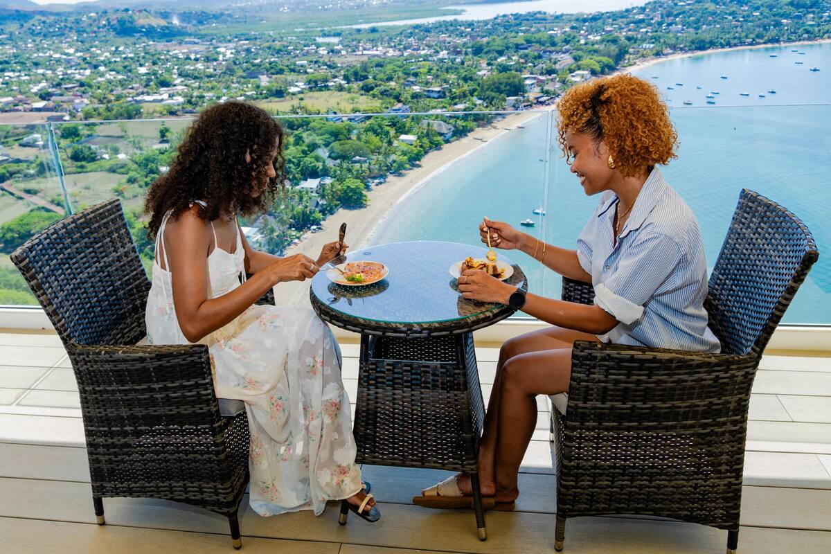 Two people dining at a table with a view of a beach and cityscape.
