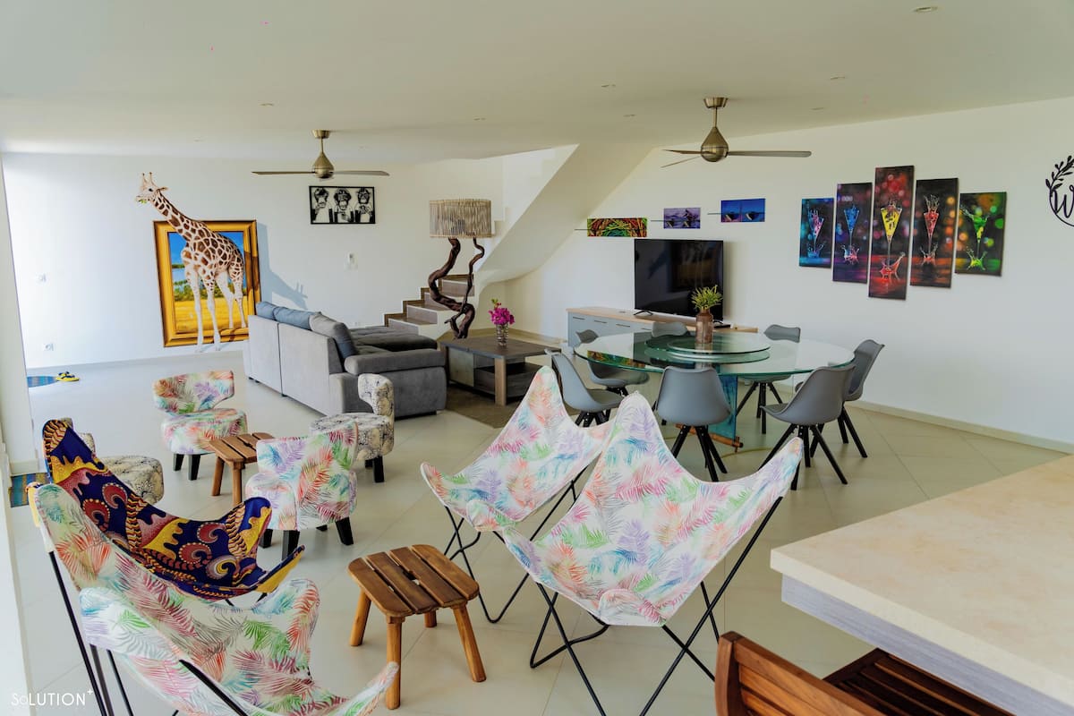 A modern living room with a sofa, chairs, a dining table, and a staircase.