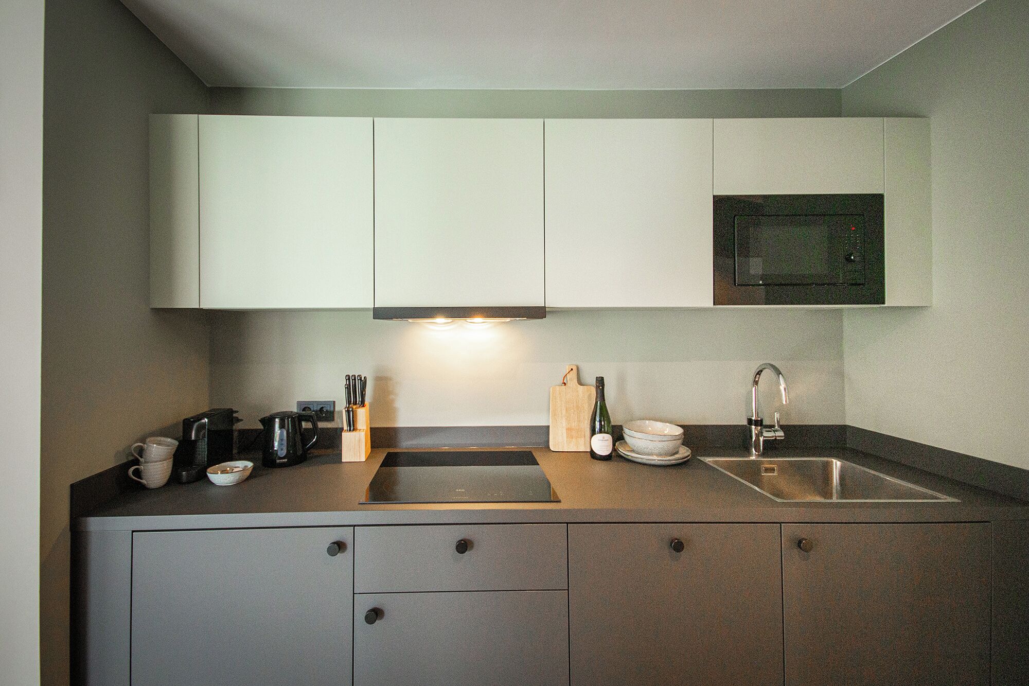 A modern kitchen with white cabinets, a black countertop, a built-in microwave, and a stainless steel sink.