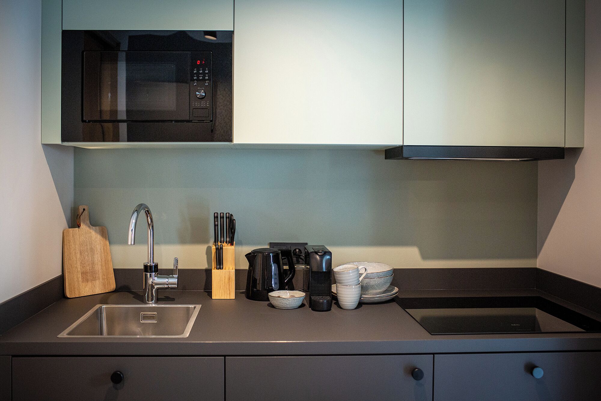 Une cuisine moderne équipée d’un four à micro-ondes encastré, d’un évier en acier inoxydable et d’une machine à café.