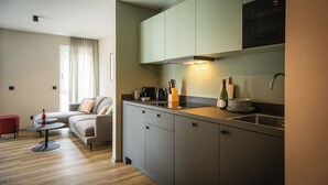 Un espacio habitable compacto con kitchenette, un sofá, una mesita y una ventana con cortinas.