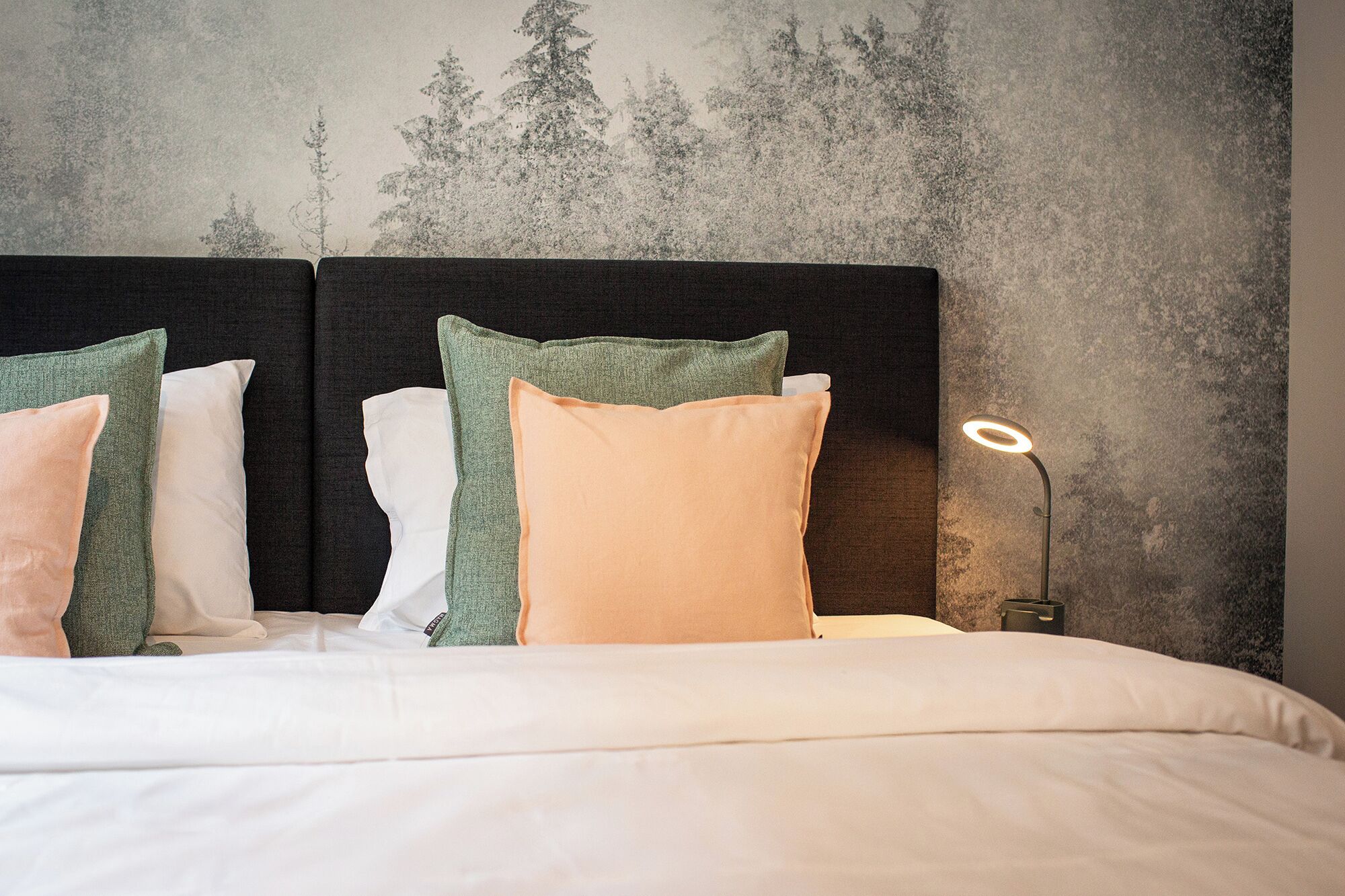 A neatly made bed with a headboard, pillows, and a bedside lamp.