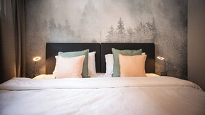 Una cama con sábanas blancas y dos almohadas, un cabecero oscuro y una pared con un mural de un bosque.