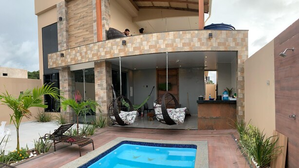 Una casa moderna de dos pisos con piscina, mobiliario exterior y un patio cubierto.