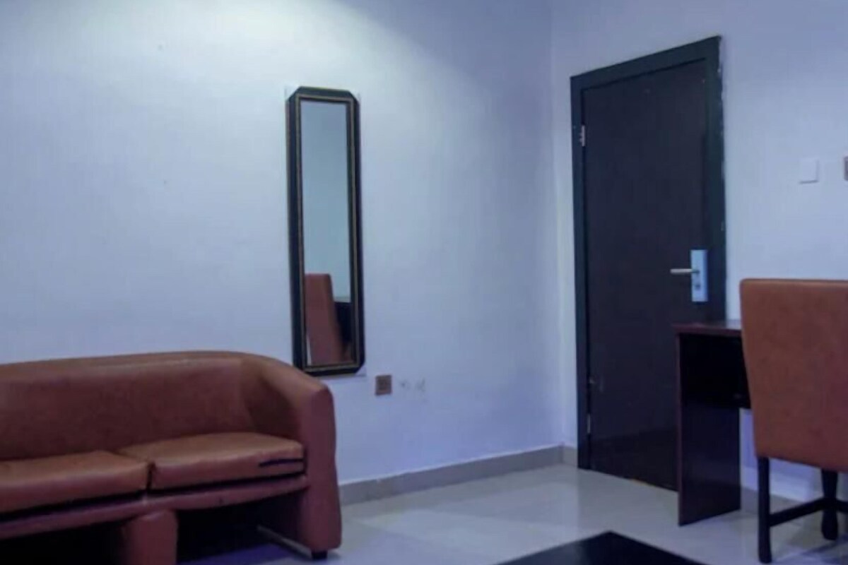 A room with a brown sofa, a black table, a mirror, and a door.