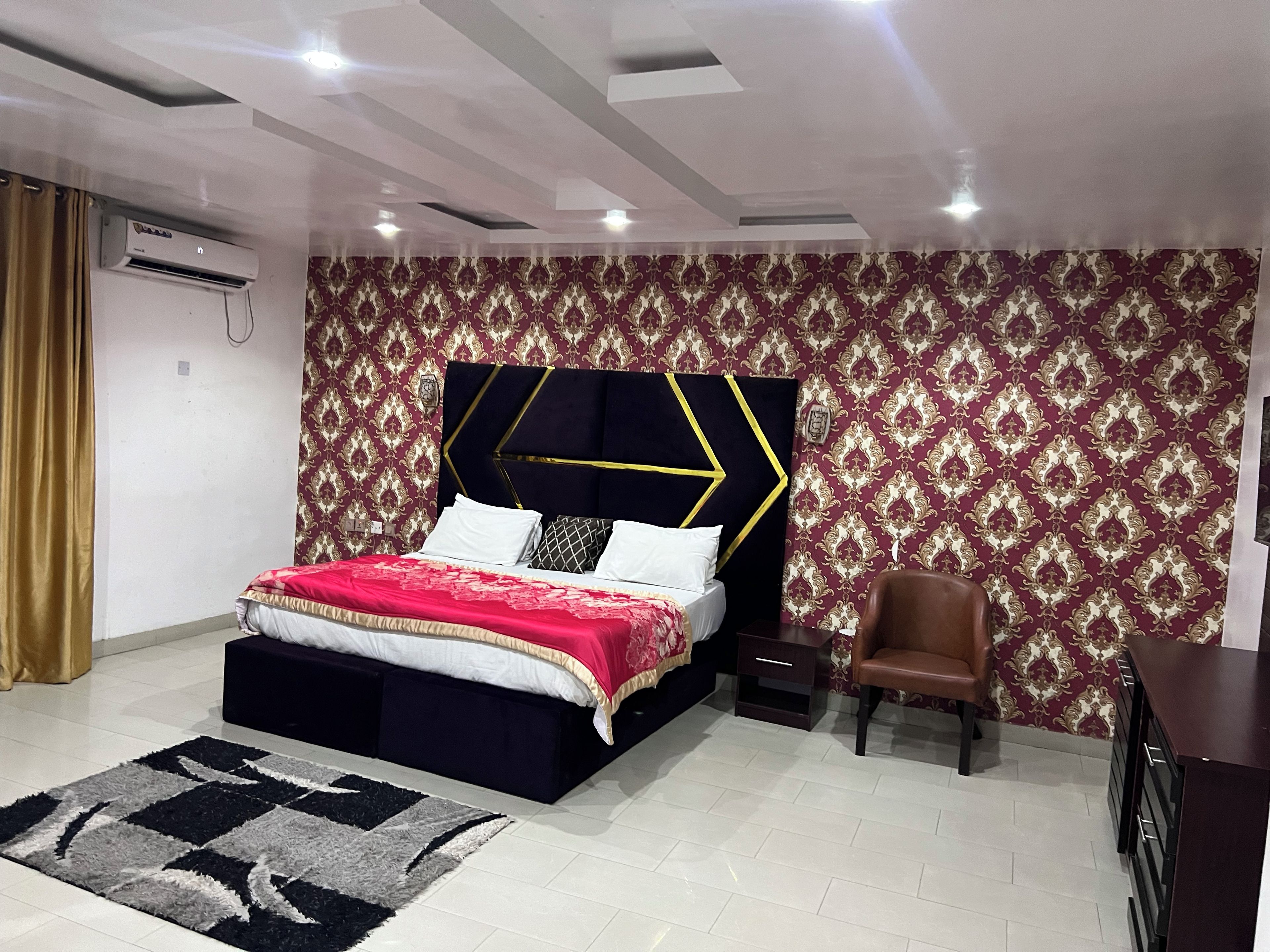 Un dormitorio con cama, una silla, cómoda y papel tapiz estampado.