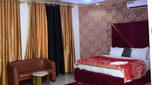 Quarto com cama, sofá, mesa redonda pequena e cortinas estampadas.