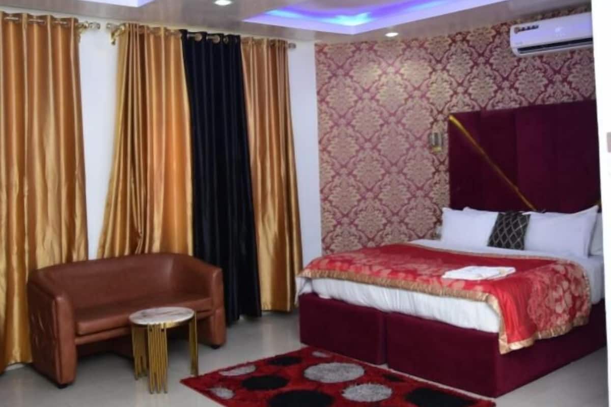 A bedroom with a bed, a sofa, a small round table, and patterned curtains.