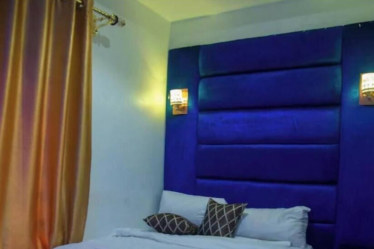 A bedroom with a blue headboard, white bedding, and two wall-mounted lights.