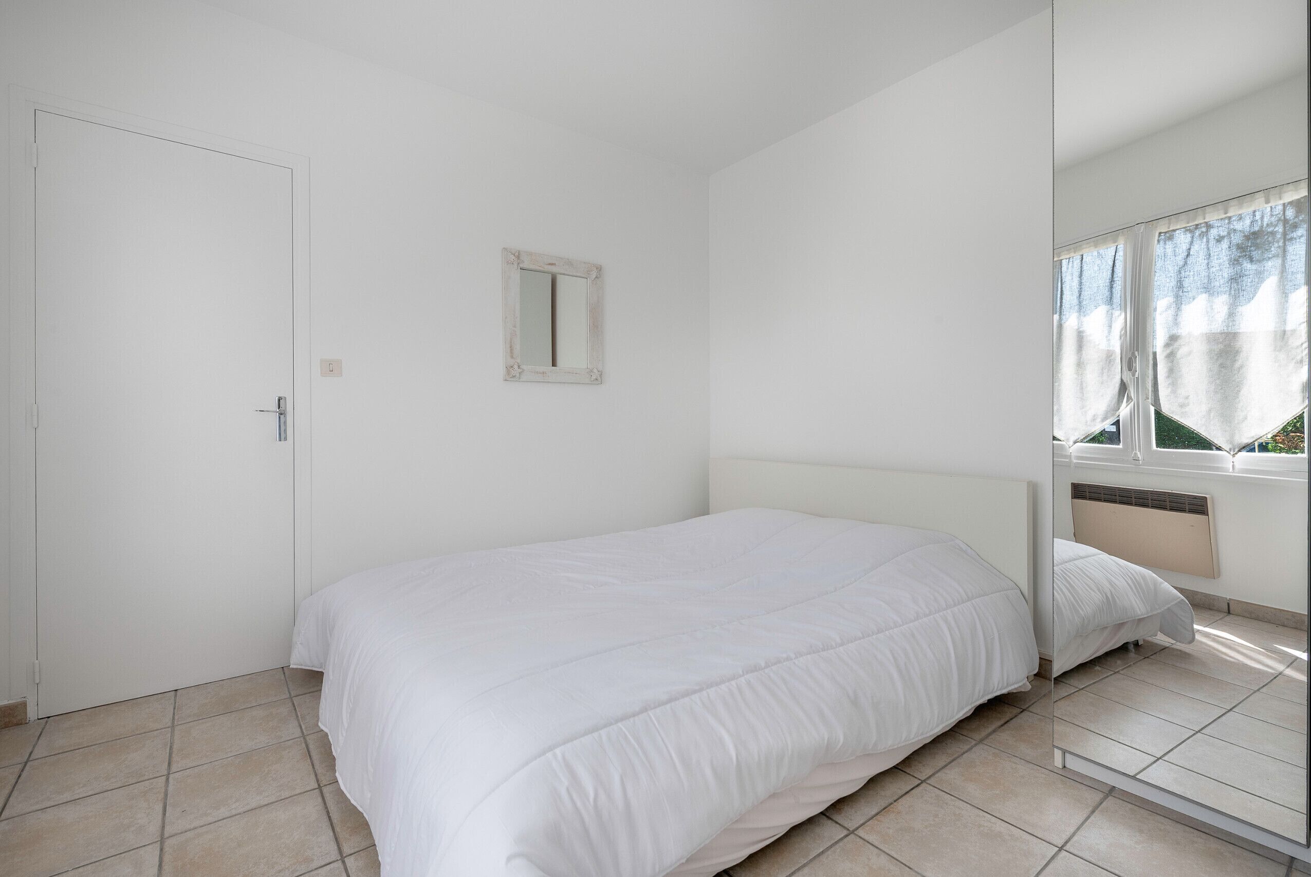 A bedroom with a bed, a door, a mirror, and a window.