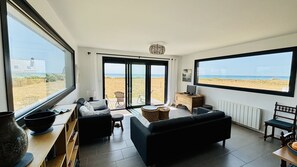 A modern living room with a view of the beach, a dining area, and a seating area with a view of the ocean. - Sea view, beach access, 6 adults and 1 child (Plovan)