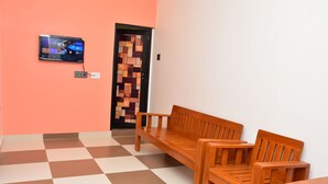 Een geruite vloer, een houten bankje, een kleine tafel, een aan de muur bevestigde televisie en een deur met houtstructuur.