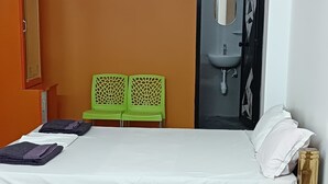 Een slaapkamer met een bed, een plafondventilator, een airconditioning, een kledingkast en een badkamer met een wastafel en spiegel.