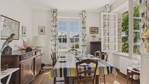 A dining room with a striped tablecloth, wooden chairs, and a view of greenery outside. - Sea view – house for 4 adults and 3 children (Bénodet)