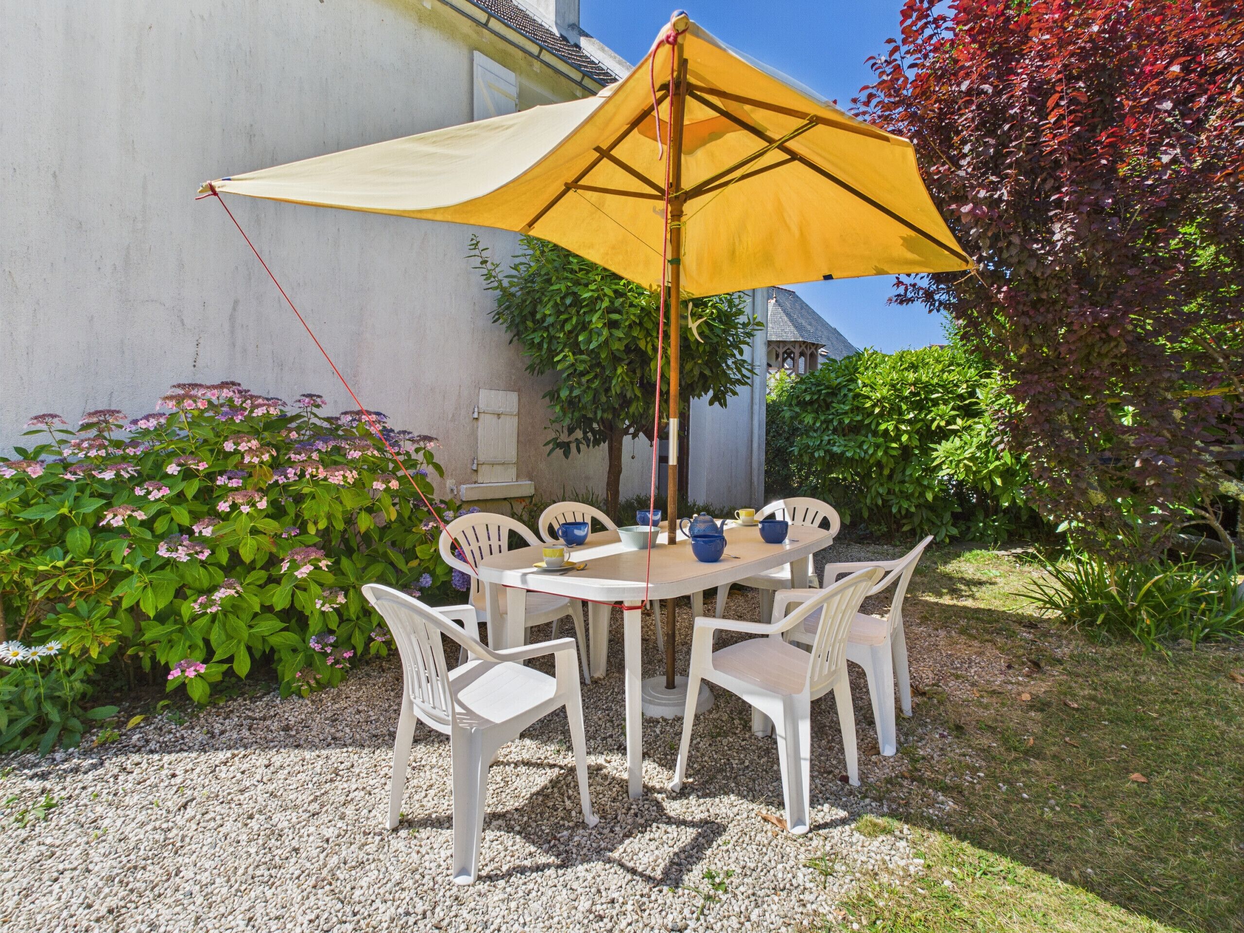 Un tavolo rotondo con sedie bianche e un ombrellone giallo in un giardino.