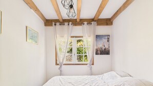 Un dormitorio con una cama grande, vigas de madera en el techo, una ventana con cortinas y dos cuadros en la pared.