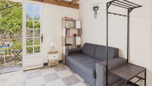 Una habitación con un sofá gris, una mesita de madera, una estantería y un tendedero metálico.