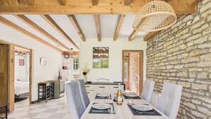 Un comedor con una mesa y sillas de madera, una araña y una pared de piedra.