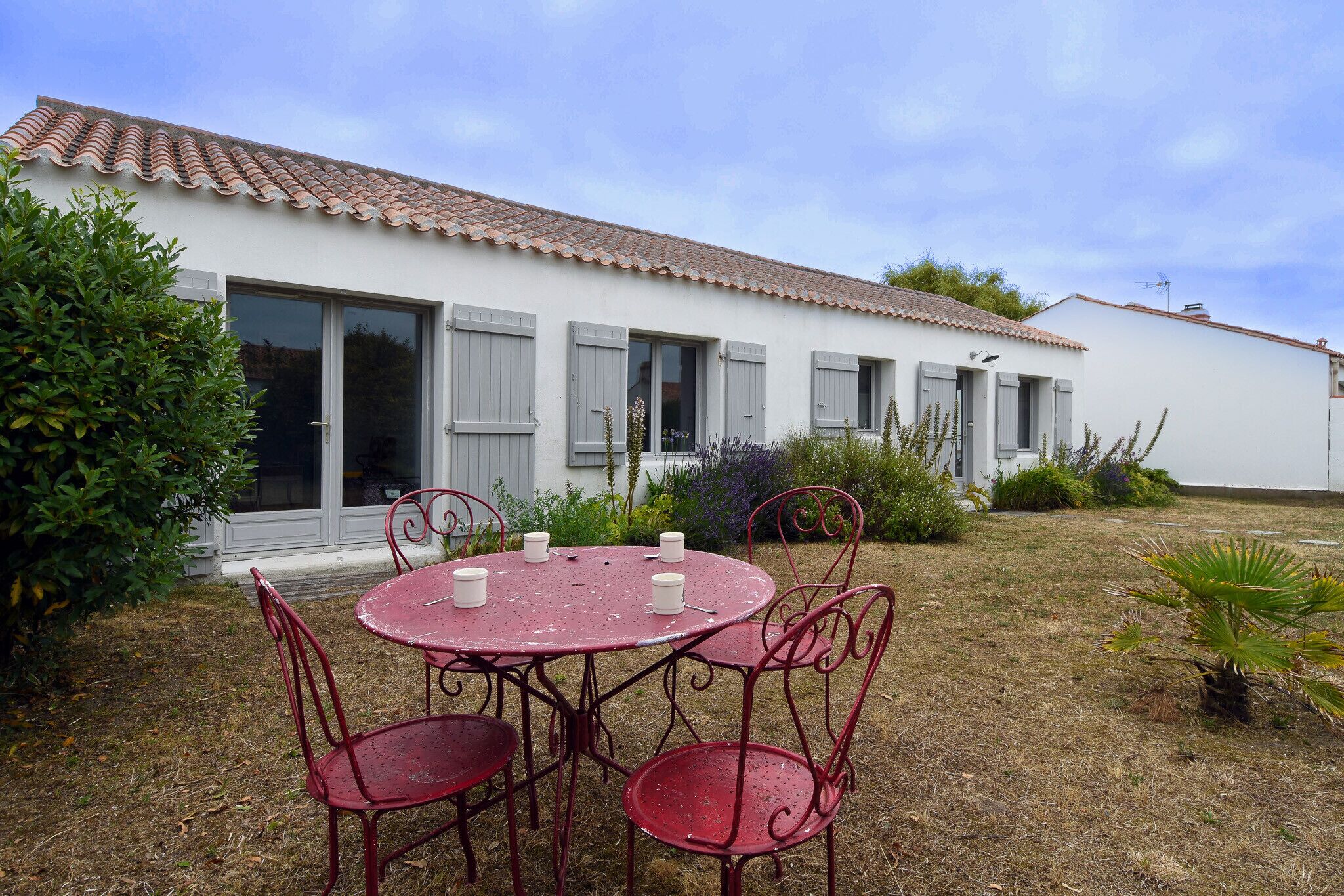 Un bâtiment blanc avec un toit en tuiles et un jardin comprenant une table ronde et des chaises en métal.