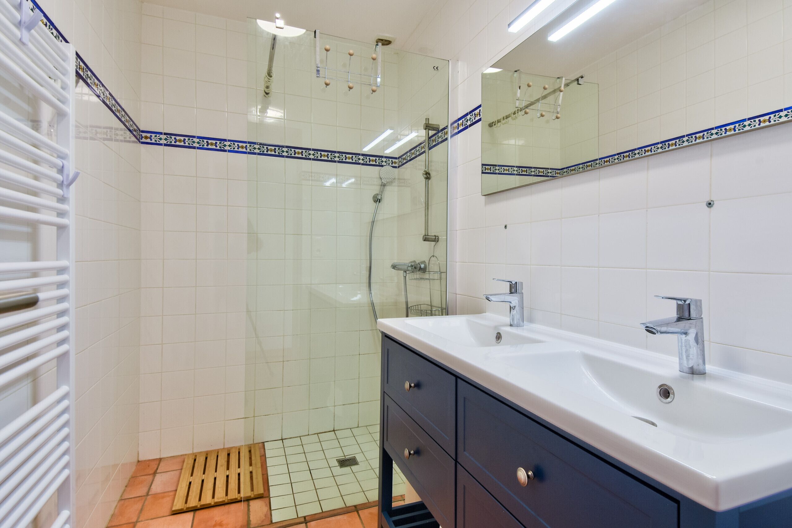 A modern bathroom with a glass-enclosed shower, a white sink with a mirror, and a tiled floor.