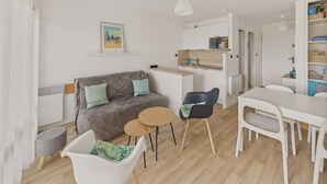 A modern living room with a grey sofa, a dining table, and a kitchen area. - Sea-view apartment for 2 adults and 3 children (Carnac)