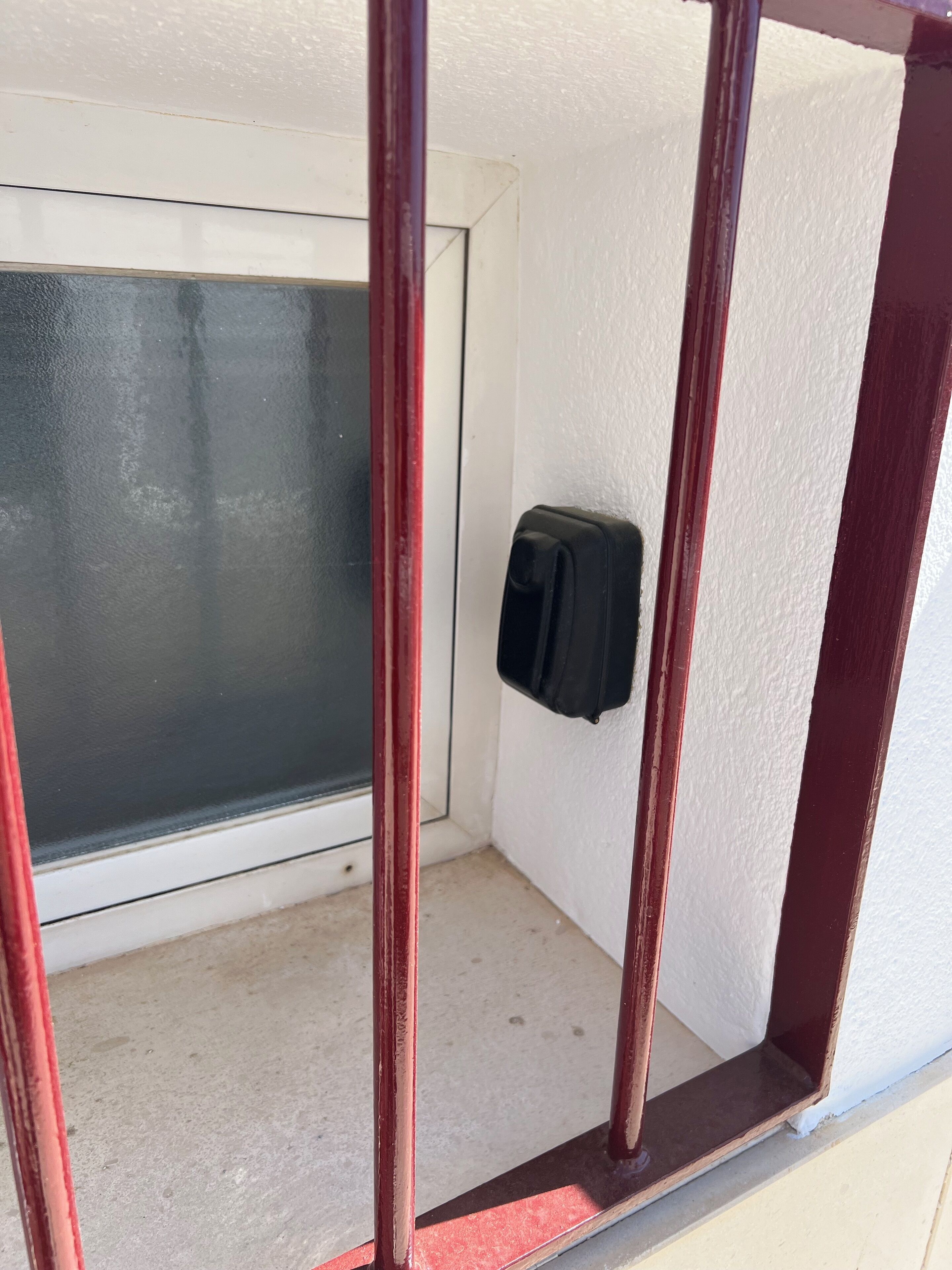 A corner of a room with a white wall, a glass door, and a black object on the wall.