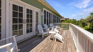 A wooden deck with white chairs and a small table, a white railing, and a green building with large windows.