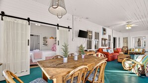 A spacious room with a wooden dining table, wicker chairs, a red sofa, and a teal floor.