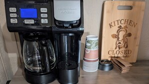 A kitchen area with a Hamilton Beach FlexBrew coffee maker, a Proctor Sable microwave, and a wooden cutting board labeled "KITCHEN CLOSED". - Cozy cabin in charming Trenton NC (Trenton)