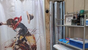 A bathroom with a shower curtain featuring a cowboy riding a horse, a metal shelf with toiletries, and a toilet tank. - Cozy cabin in charming Trenton NC (Trenton)