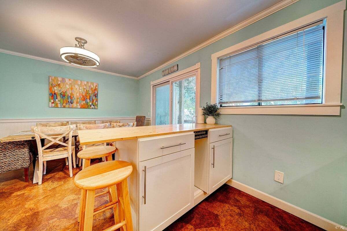 Una cocina con una isla de madera, armarios blancos y una ventana con persianas.