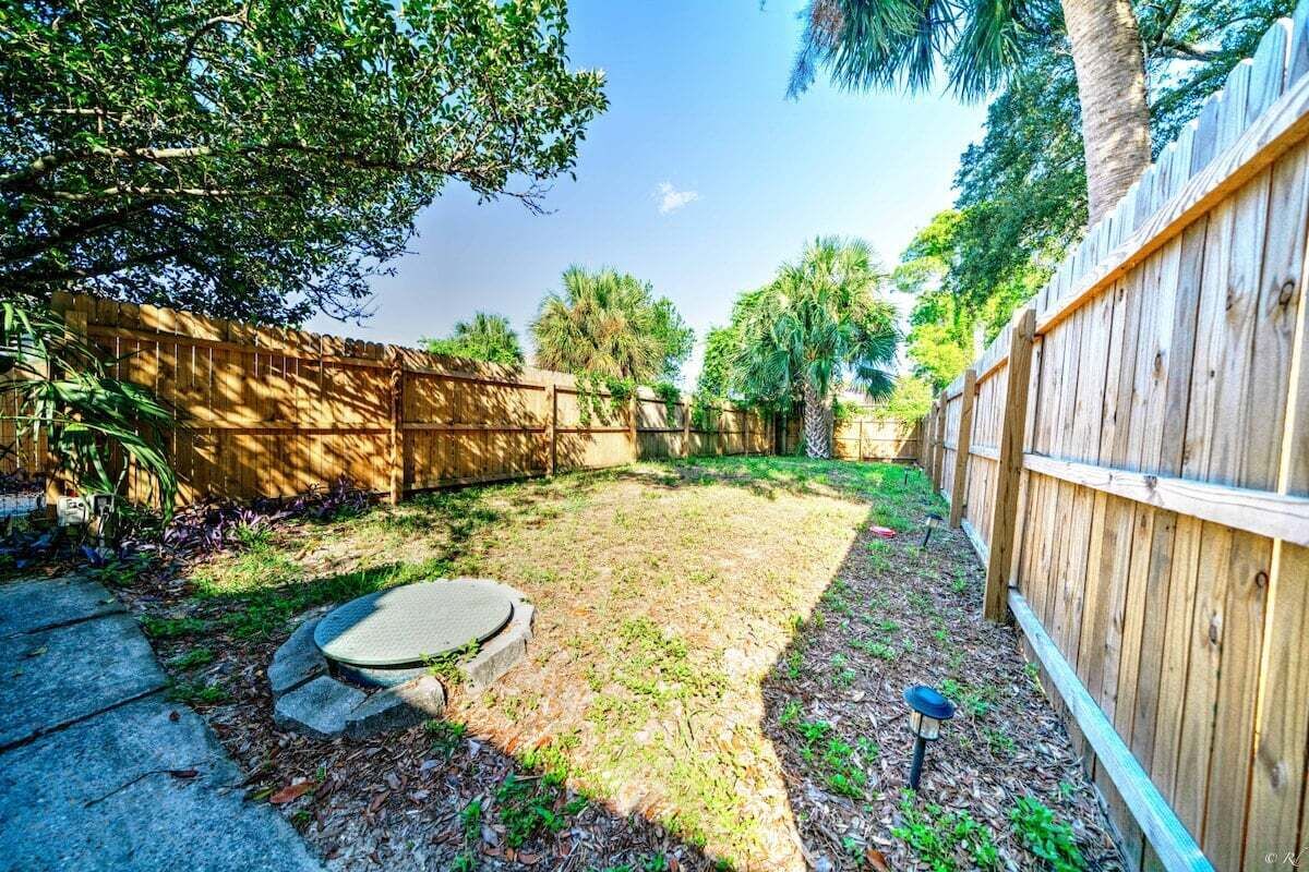 A backyard with a wooden fence, a concrete pad, and a small garden area.
