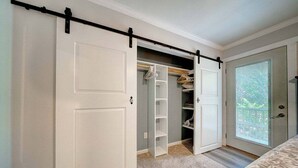 A bedroom with a sliding closet door, a bed, and a window with a view of greenery.