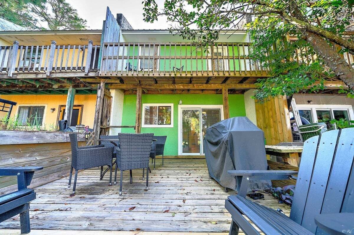 A deck with outdoor furniture, a covered grill, and a green building with a wooden balcony.