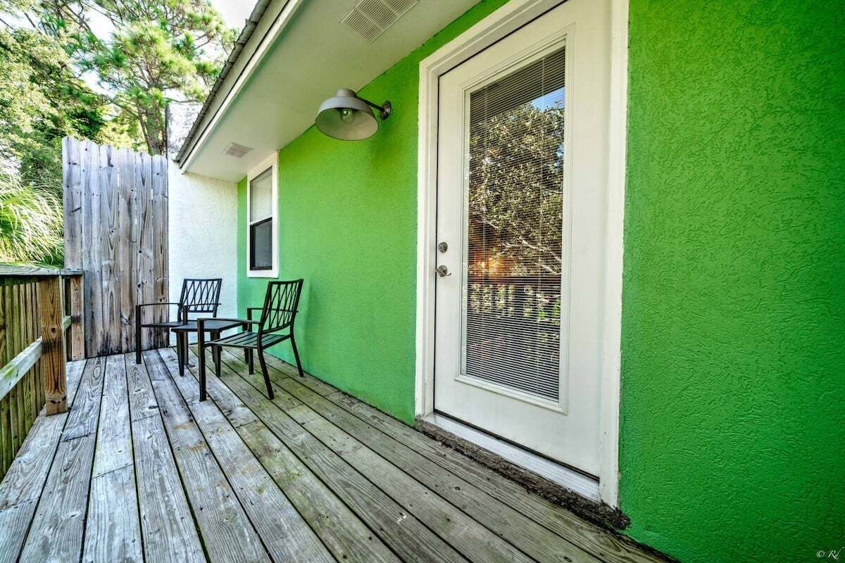 A wooden deck with a green wall and a white door with a window.