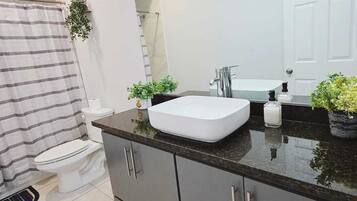 A modern bathroom with a white sink, dark cabinets, a large mirror, and a shower area.