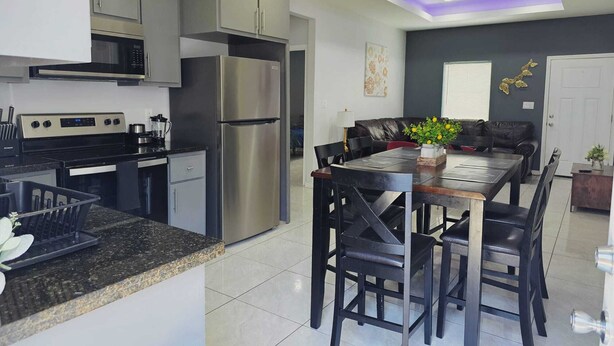 A modern kitchen with stainless steel appliances, a dining area with a dark wooden table and chairs, and a living room with a leather sofa and decorative wall art.
