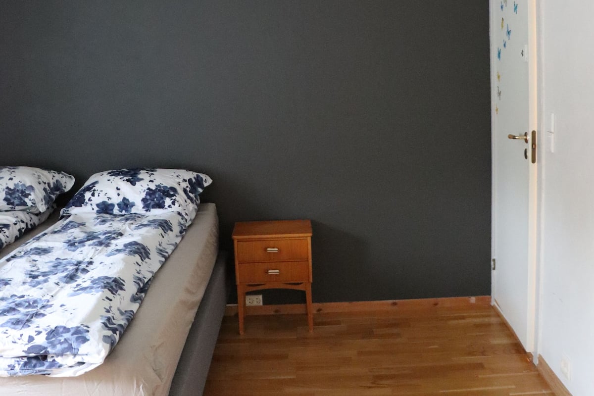 A bedroom with a bed, a nightstand, a wooden floor, and a ceiling fan.