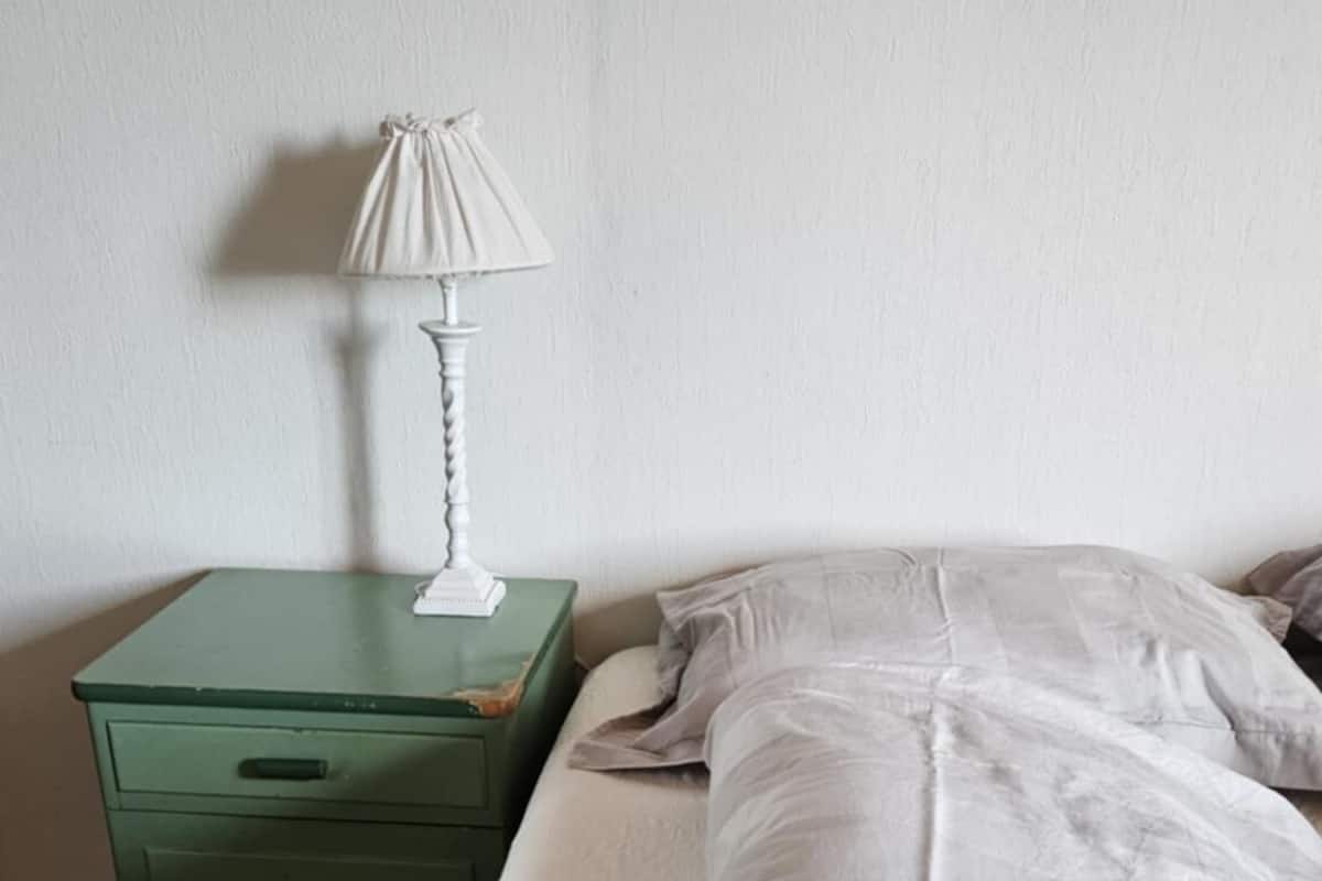 A room with a bed, a green nightstand, and a white lamp.