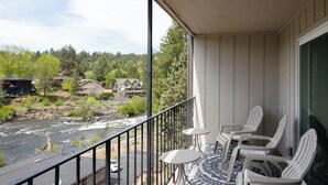 Un balcon avec des chaises blanches et une table, d’où l’on a vue sur une rivière et des maisons.