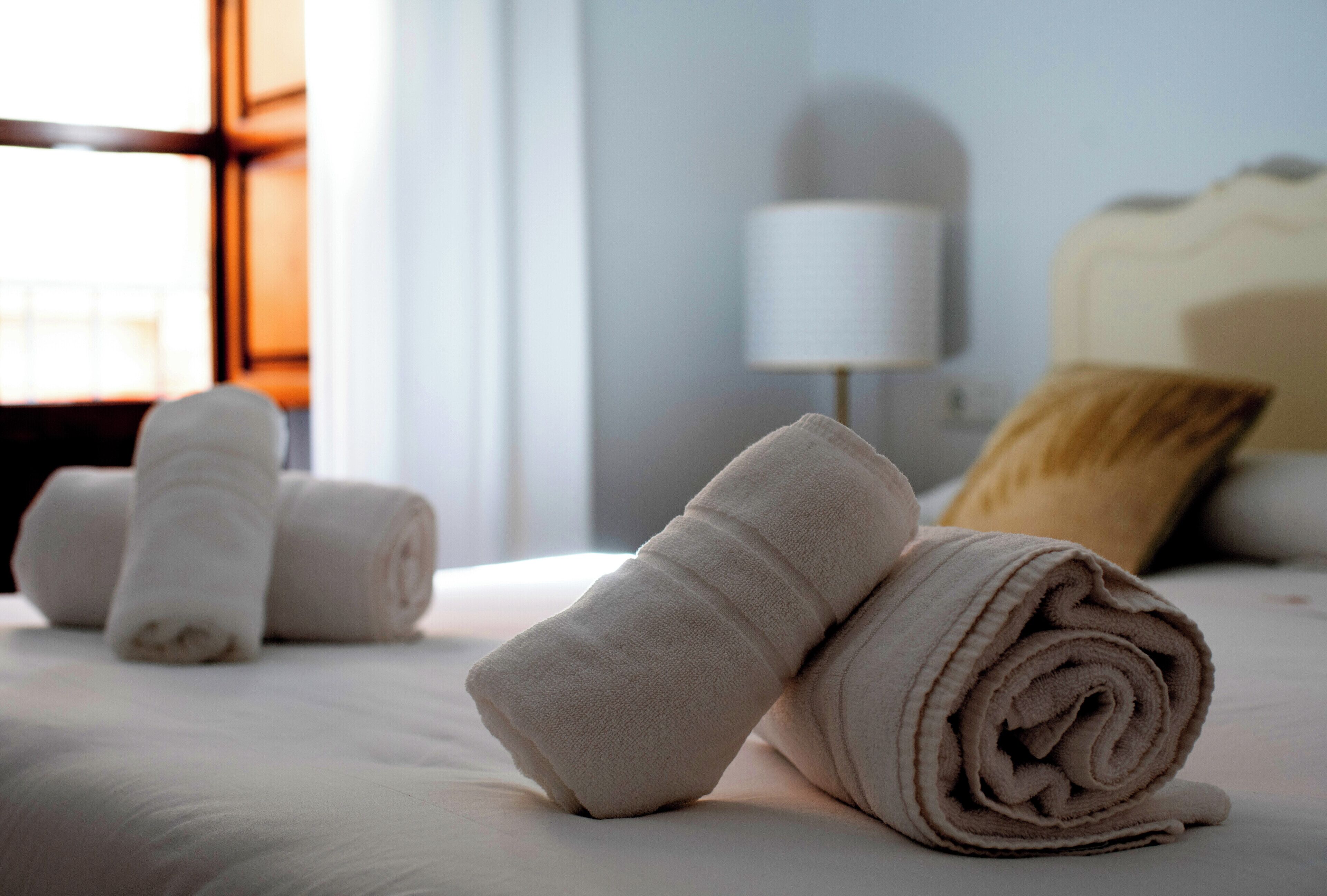 A neatly made bed with rolled towels and a lamp in the background.