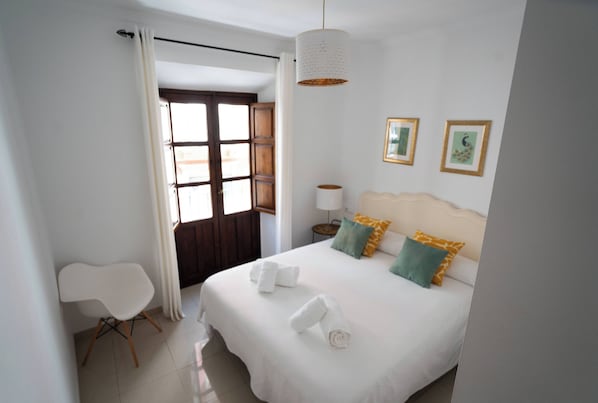 A hotel room with a bed, a chair, a window with curtains, a bedside table, and wall art. - El Marqués San Juan (Málaga)